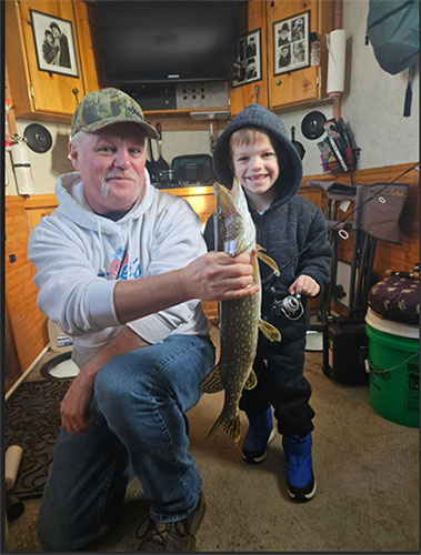 Grandpa and his fishing buddy showing off a fish caught in the “cool” fishing house