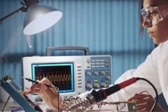 Woman using soldering iron and oscilloscope