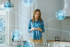 Woman using an IoT device in a kitchen. Holographic nodes with illustrations of various functions (turning on water, heating a coffee pot) surround her connected to the device by dashed lines